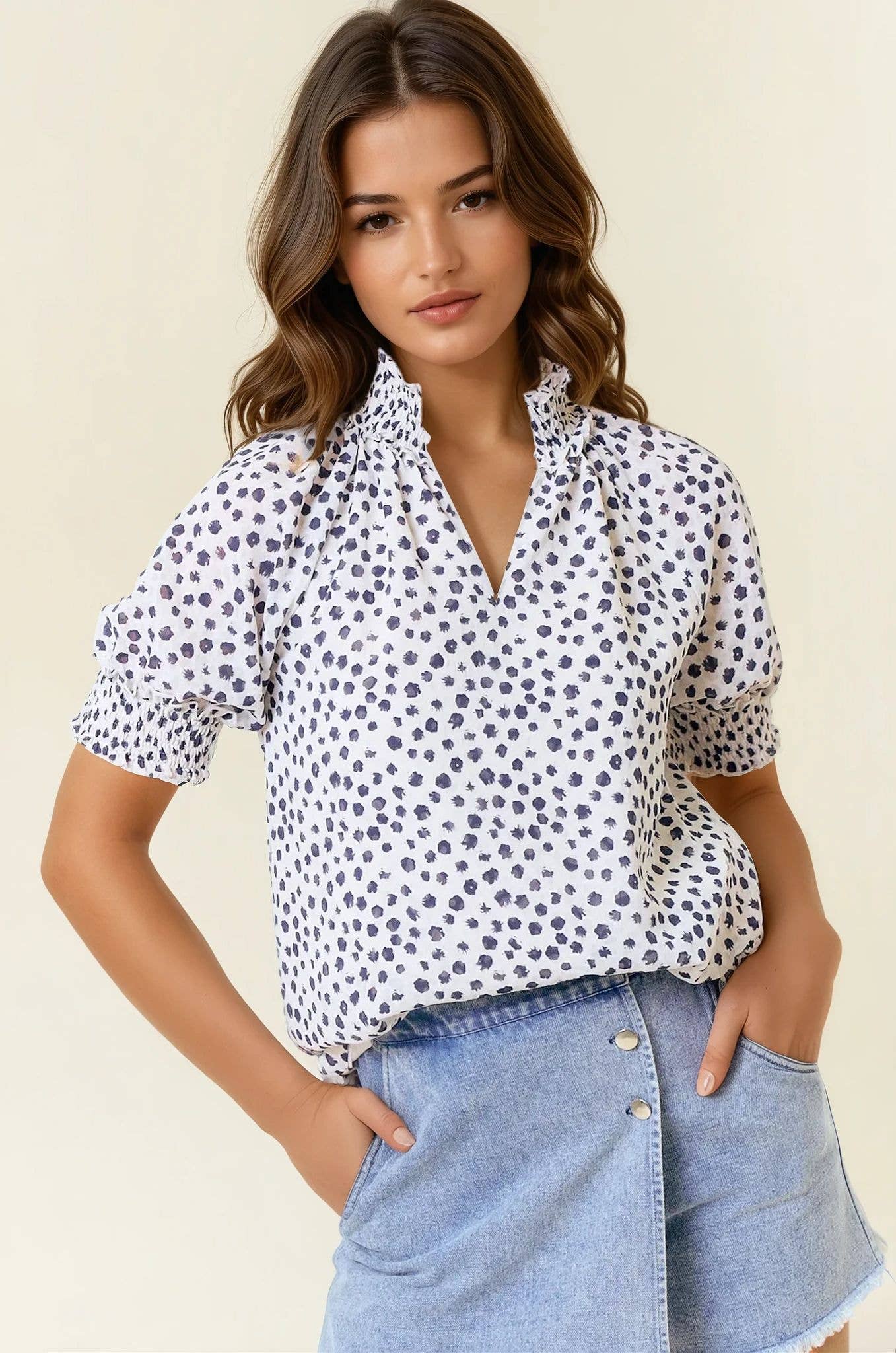 Woman wearing a white blouse with black polka dots and a denim skirt on a beige background