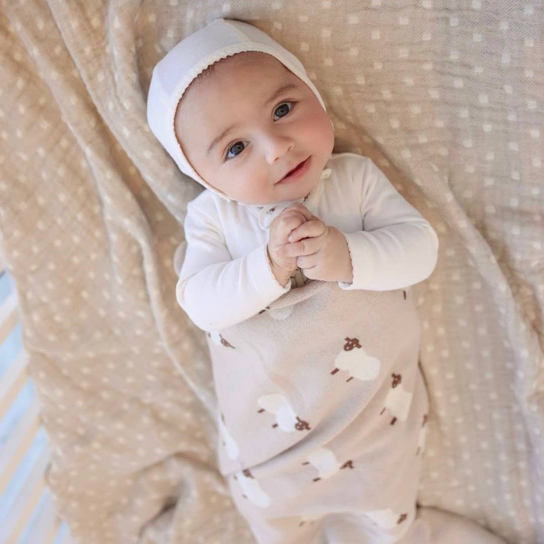 Baby wearing a white hooded outfit with bear patterns on a soft beige blanket.
