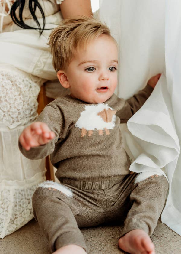 Baby wearing a brown outfit with white cloud design sitting on a couch.