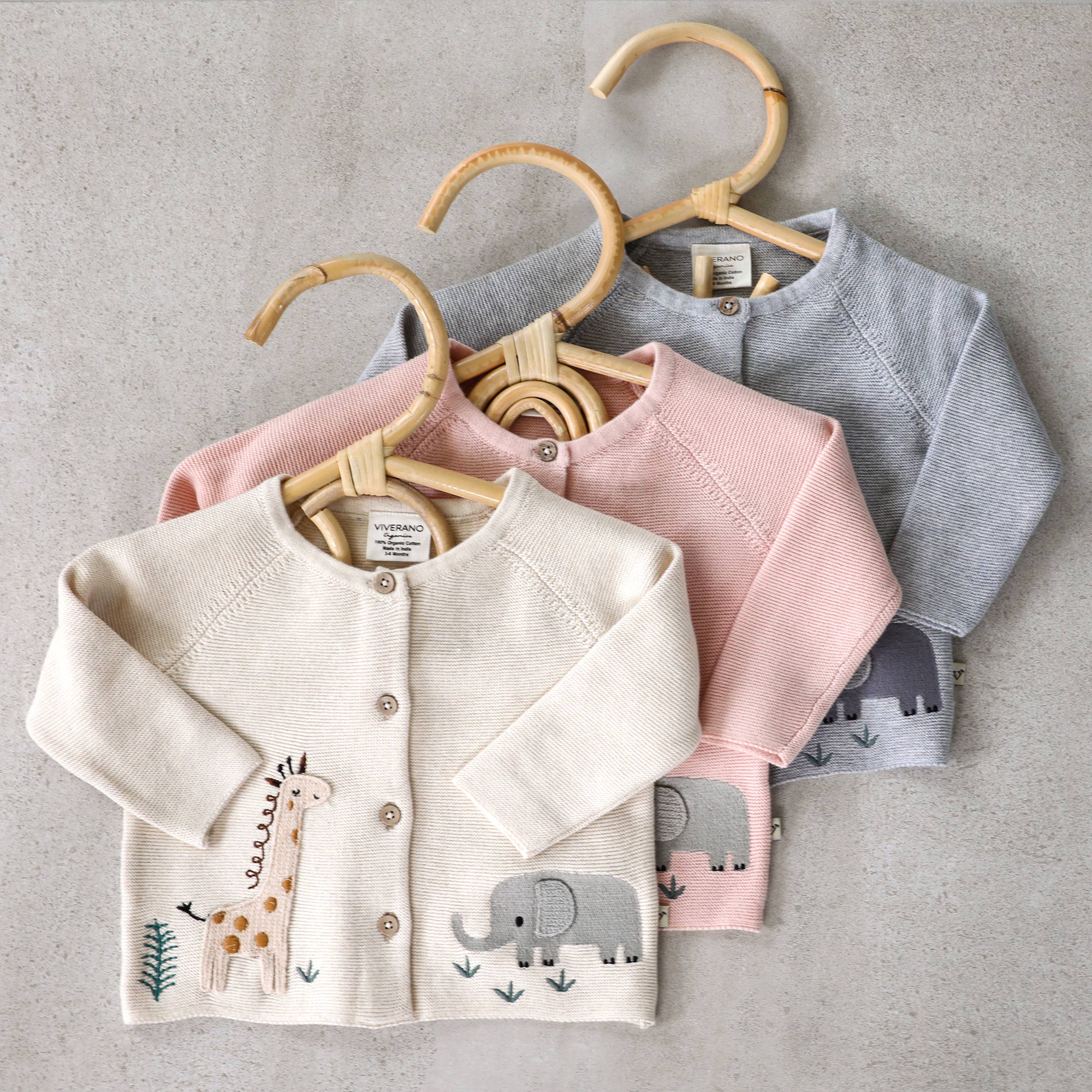 Three children's cardigans on hangers against a gray background