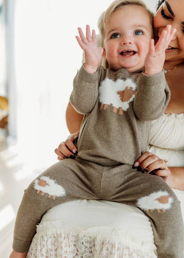 Baby wearing a brown distressed outfit with a cloud design, sitting on a white surface.