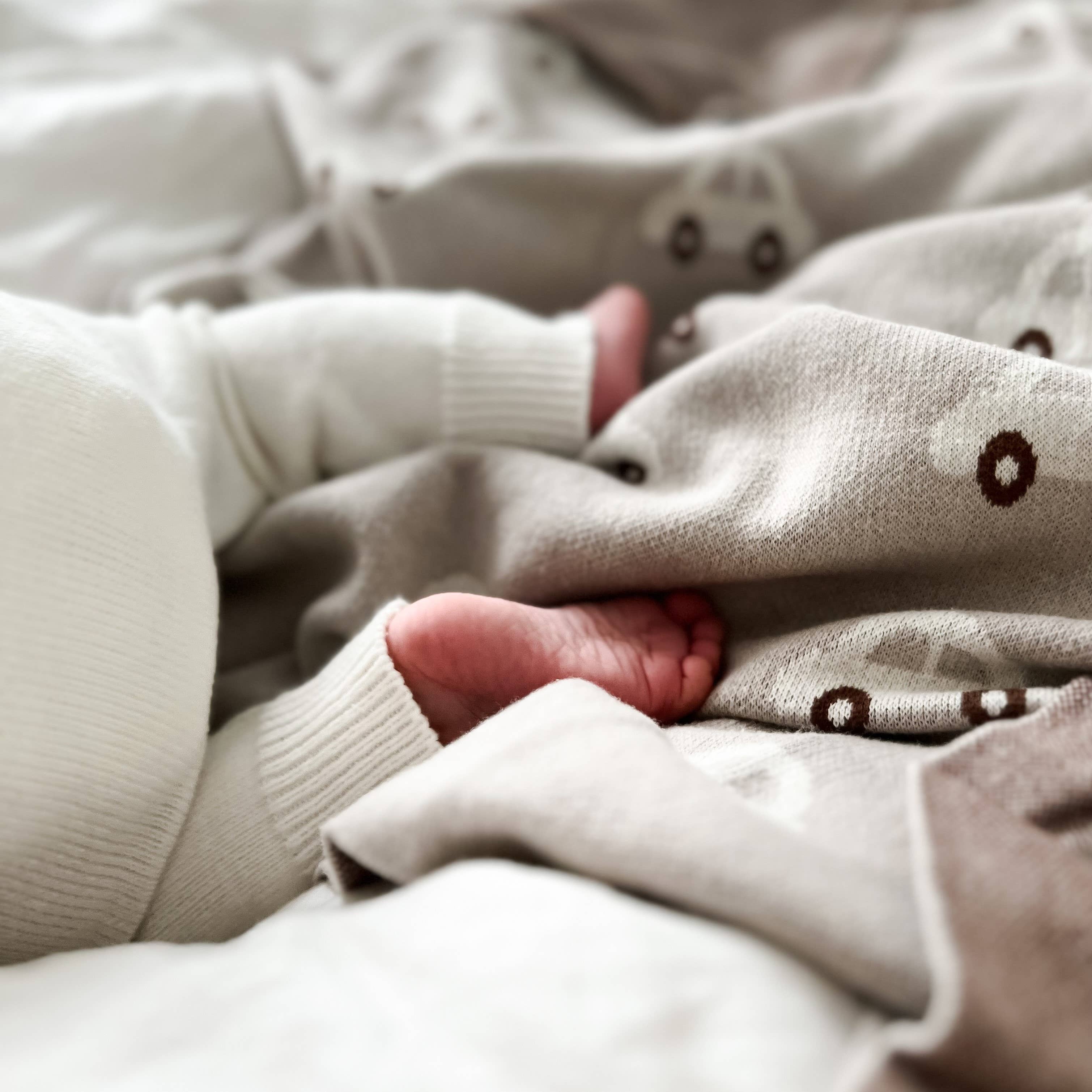Close-up of a baby's hand and foot in a soft, beige sweater with brown polka dots.