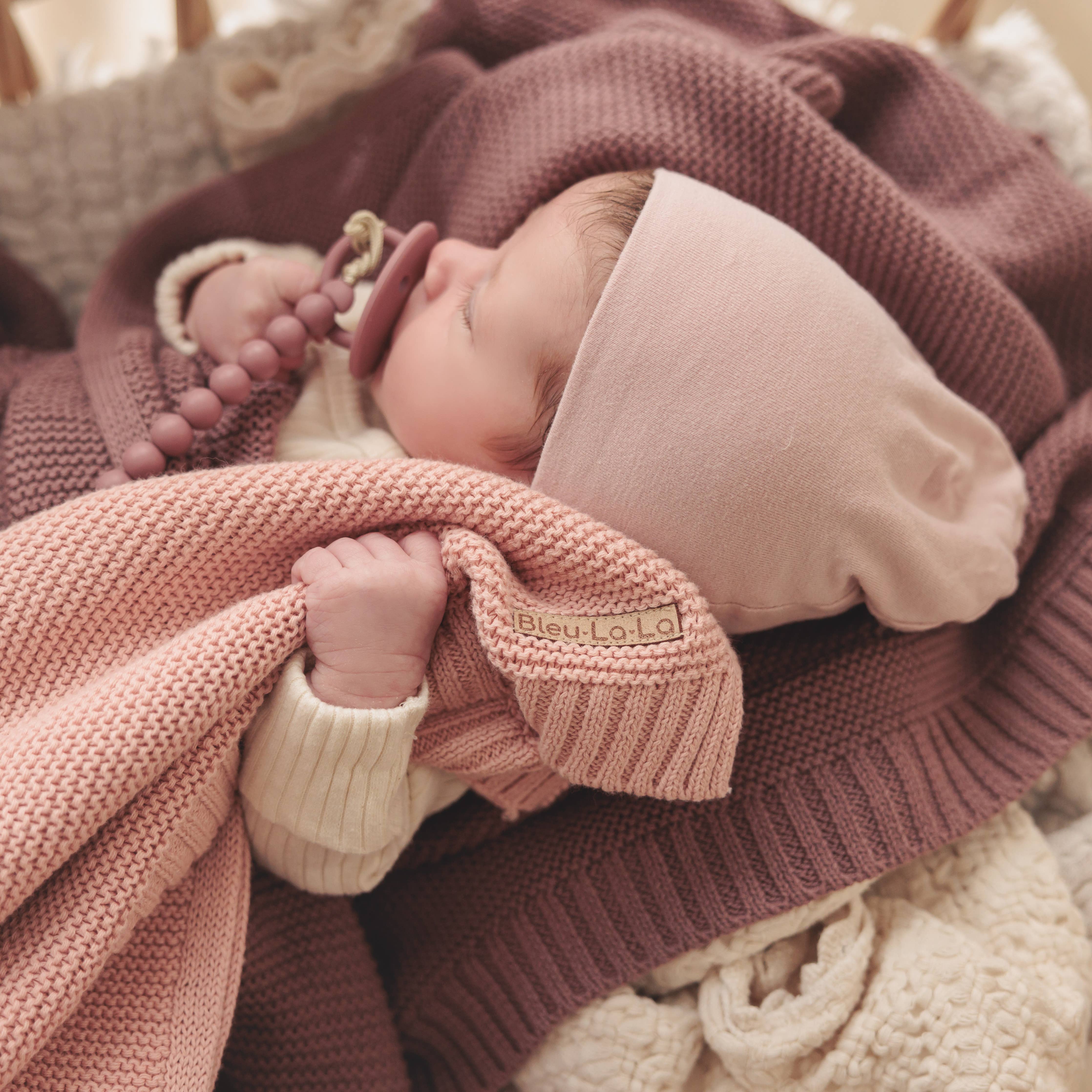 Newborn baby wrapped in pink and purple blankets with a blurred background